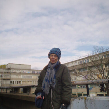 Still from Here Us Now - Sasha Winslow stands outside a London housing estate