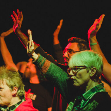 A group of people in a performance raise their hands in defiance
